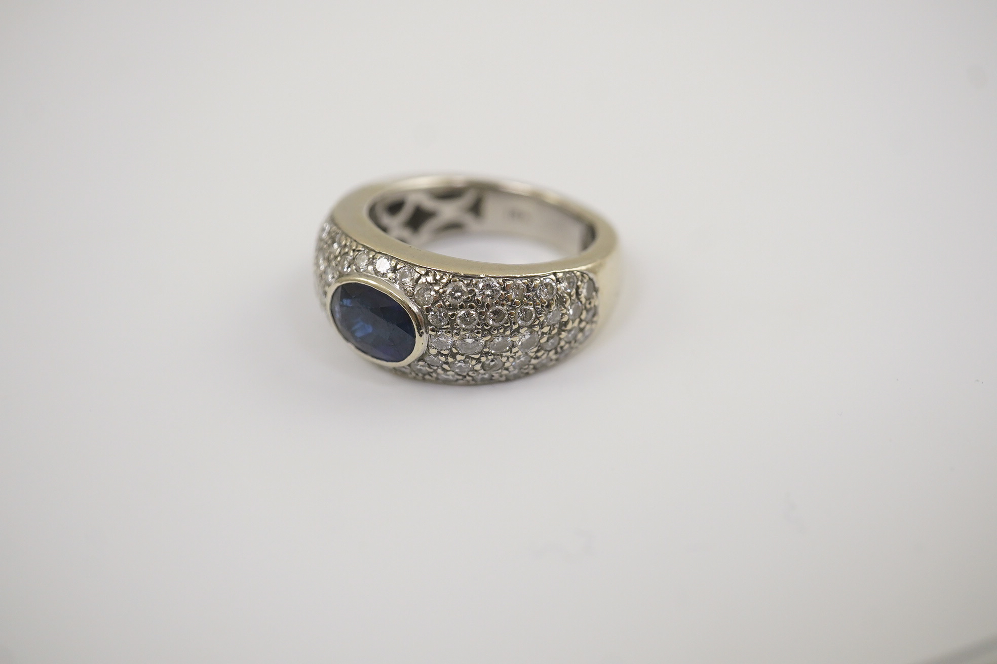 A modern 18k white gold and gypsy set single stone oval cut sapphire set ring, with pave diamond set shoulders